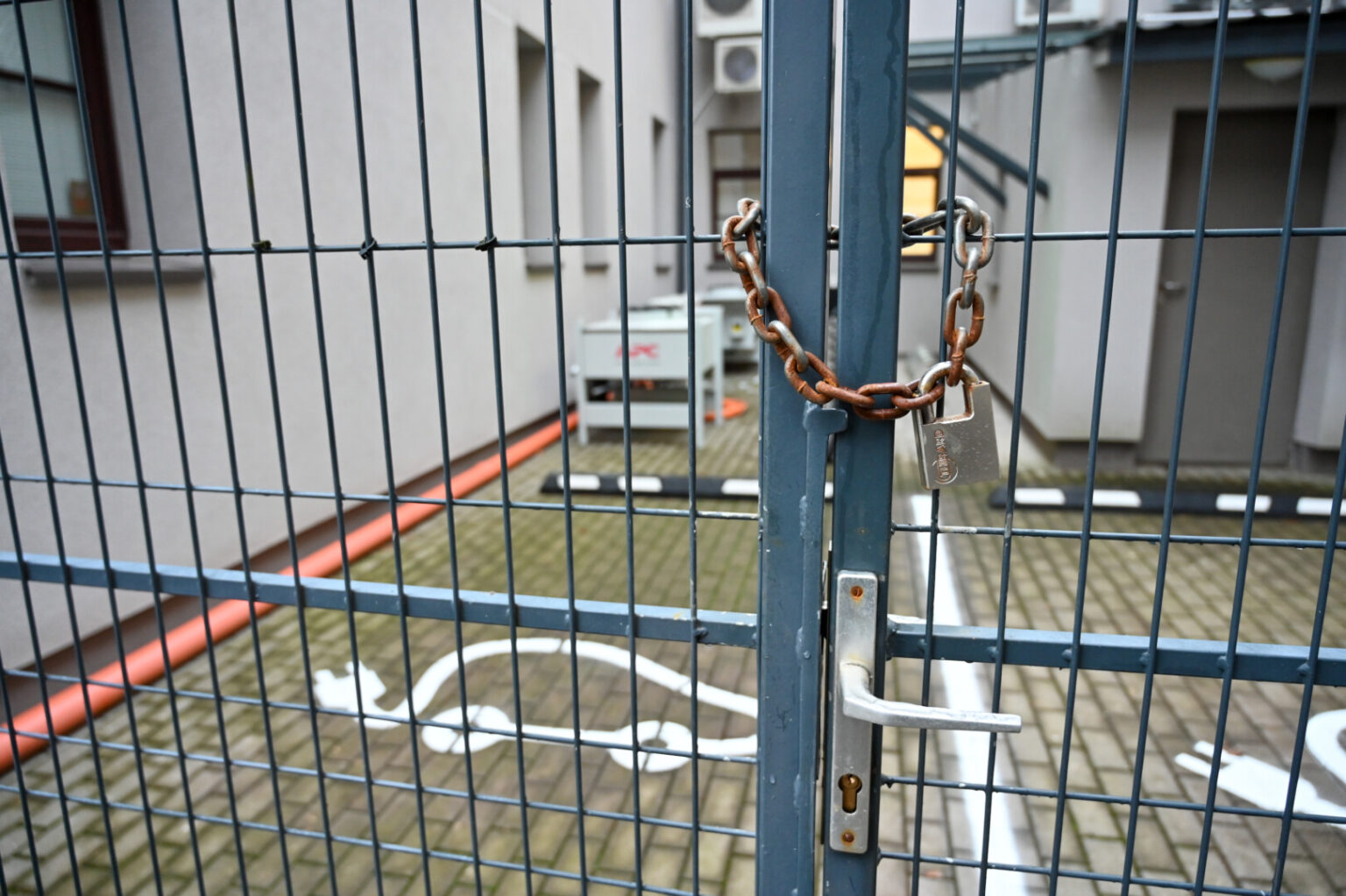 Panevėžio teritorinės ligonių kasos kieme vasarą įrengtą elektromobilių įkrovos stotelę saugo metalinė tvora su grandine ir pakabinta spyna.