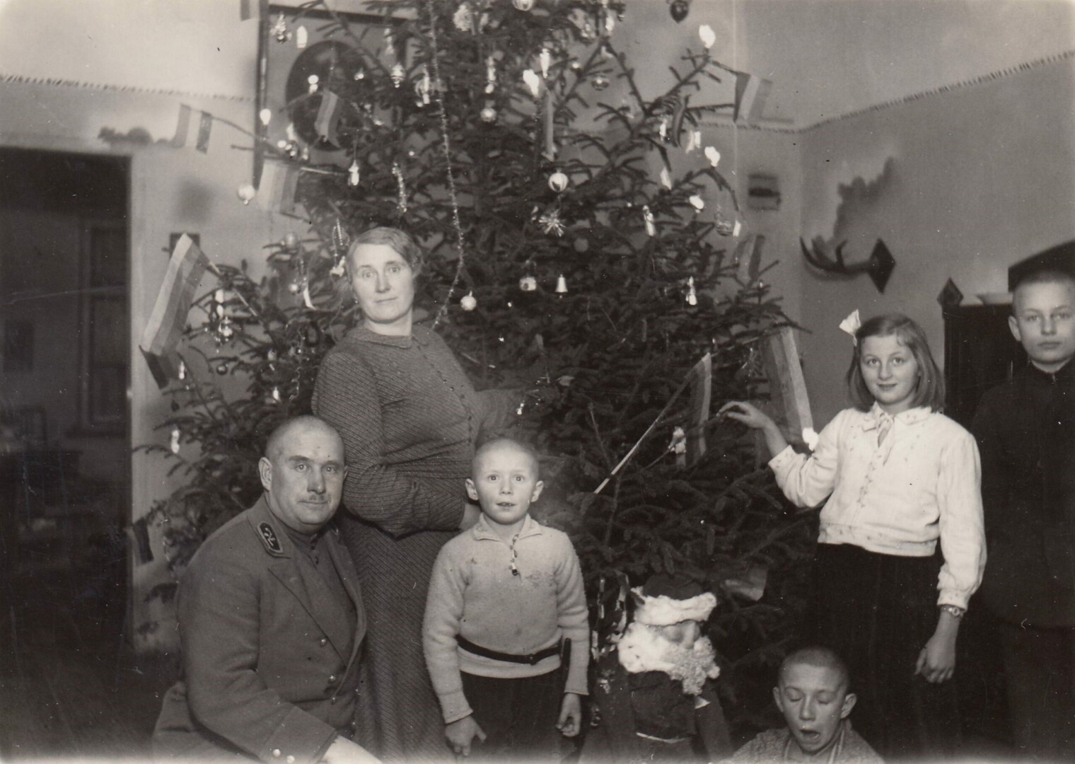 Panevėžio apskrities Žalgirio (Žaliosios) miškų urėdo Aleksandro Sakalausko šeima prie žaisliukais ir trispalvėmis papuoštos Kalėdų eglutės. Panevėžys. Apie 1935 metus. Panevėžio apskrities Gabrielės Petkevičaitės-Bitės viešoji biblioteka, Aleksandro Sakalausko šeimos skaitmeninis archyvas